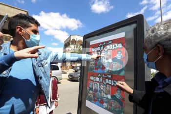 ليبيون يشيرون إلى ملصق يصور أفرادًا من عائلة ميليشيا الكانيات التي روعت ترهونة، حيث قاد ستة إخوة من عائلة الكاني حملة قمع وقتل للمعارضين في البلدة. المصدر أ ف ب